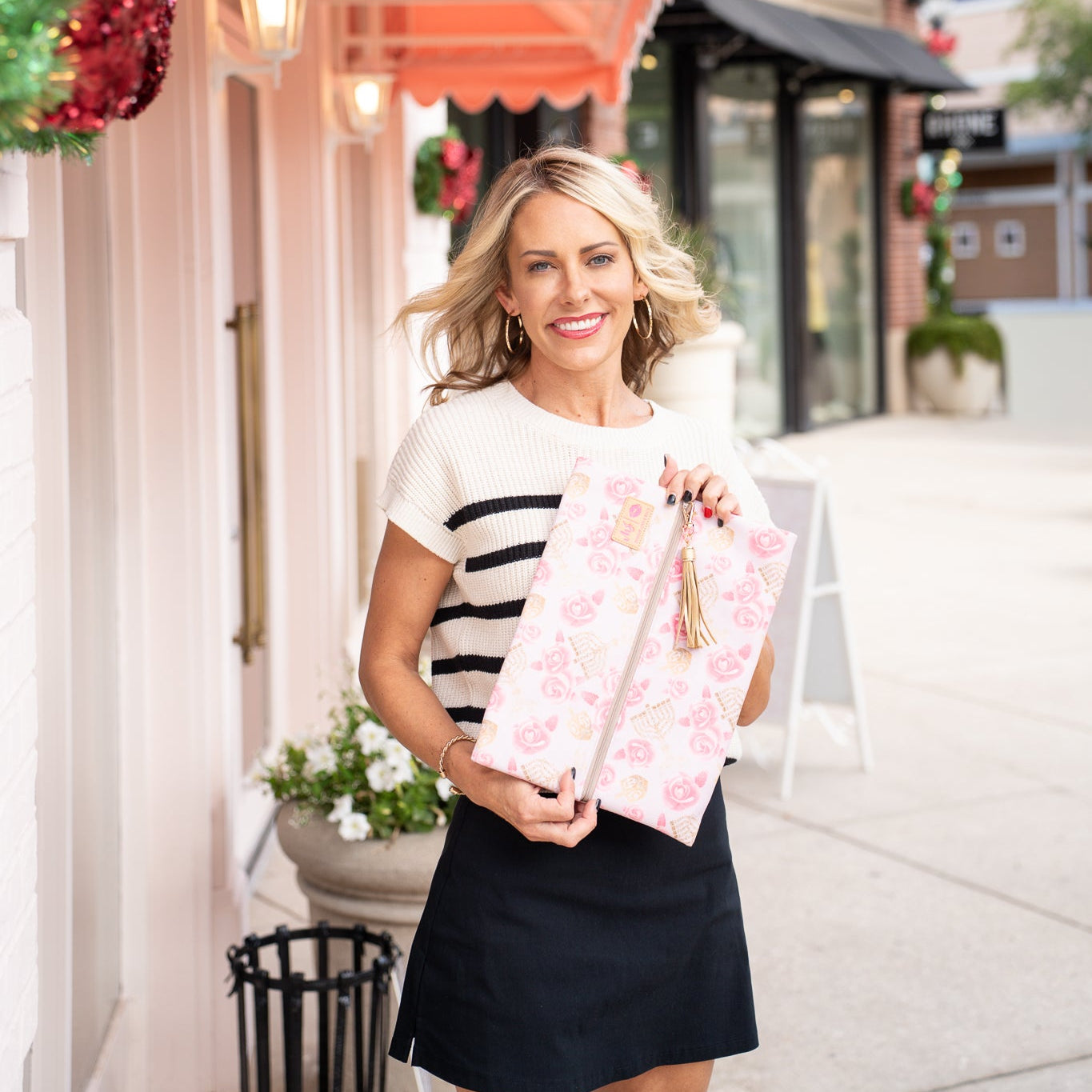Woman holding pink gift boxes in front of a store with a pink awning.
